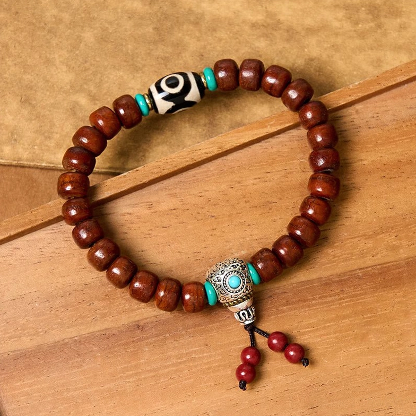 Three-eye Dzi wooden luck bracelet with black-white Dzi bead, turquoise spacers, and Tibetan silver clasp on light wooden table