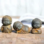 Three piece Buddha statue set featuring standing, sitting, and reclining Buddha figurines with rustic iron powder finish on wooden table with open book