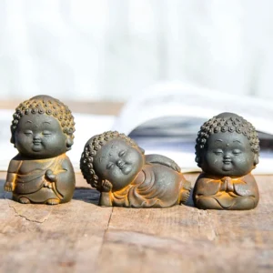 Three piece Buddha statue set featuring standing, sitting, and reclining Buddha figurines with rustic iron powder finish on wooden table with open book