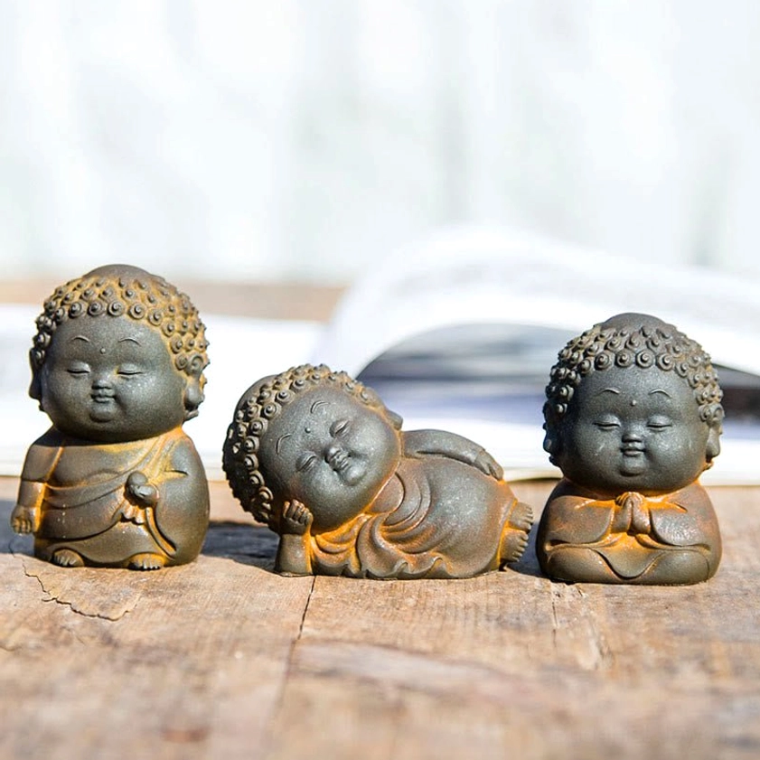Three piece Buddha statue set featuring standing, sitting, and reclining Buddha figurines with rustic iron powder finish on wooden table with open book