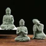 Set of three handcrafted green sandstone Buddha statues with different meditation poses displayed on natural pebbles
