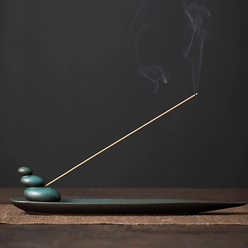 Three Stones ceramic incense holder with lit incense stick on dark wooden table, showing stacked stone design and matte teal glaze