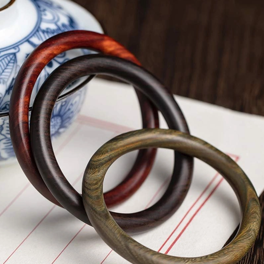 Three Buddhist wood bangles flat lay - red sandalwood, ebony, and green sandalwood variants with blue porcelain