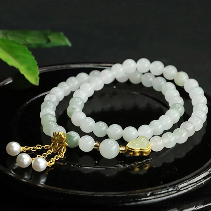 Pale green Tianshan jade bracelet with lotus-shaped gold clasp and two white pearl pendants on black ceramic tray with green leaf