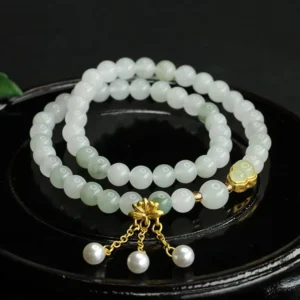 Tianshan jade lotus double circle bracelet with pearl pendants on black ceramic tray, top view showing pale green jade beads and gold clasp