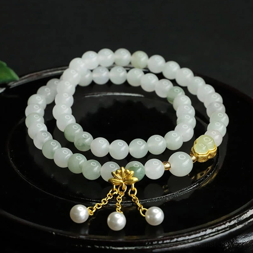 Tianshan jade lotus double circle bracelet with pearl pendants on black ceramic tray, top view showing pale green jade beads and gold clasp