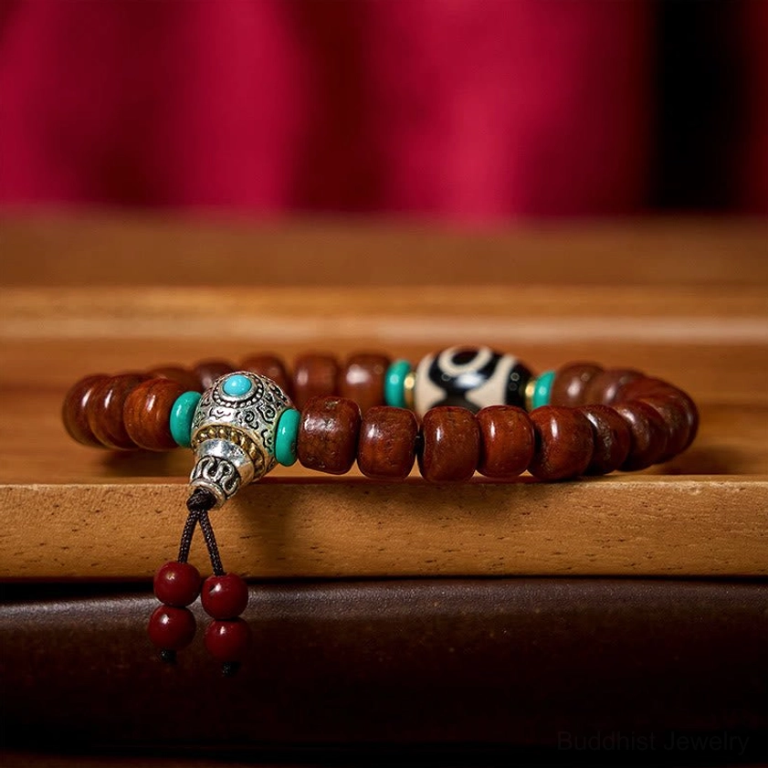 Stacked Tibetan wooden bone bead bracelets with Dzi bead, silver guru bead, and red tassel on wooden table with red backdrop