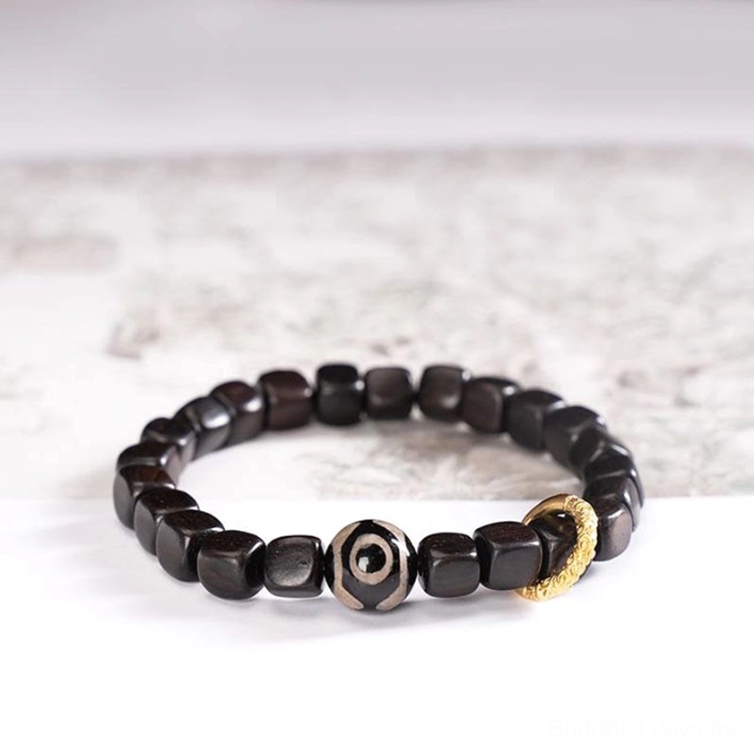 Tibetan ebony dzi bead bracelet with cubic dark wood beads, single-eye dzi bead, and gold copper accent ring displayed flat