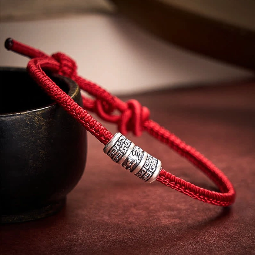 Tibetan-inspired red string protection bracelet with adjustable knot closure and engraved silver bead detail