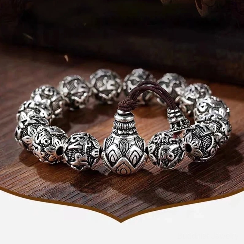 Tibetan lotus-carved guru bead mala bracelet on wooden desktop tray showing aged silver-black finish and full mantra engravings