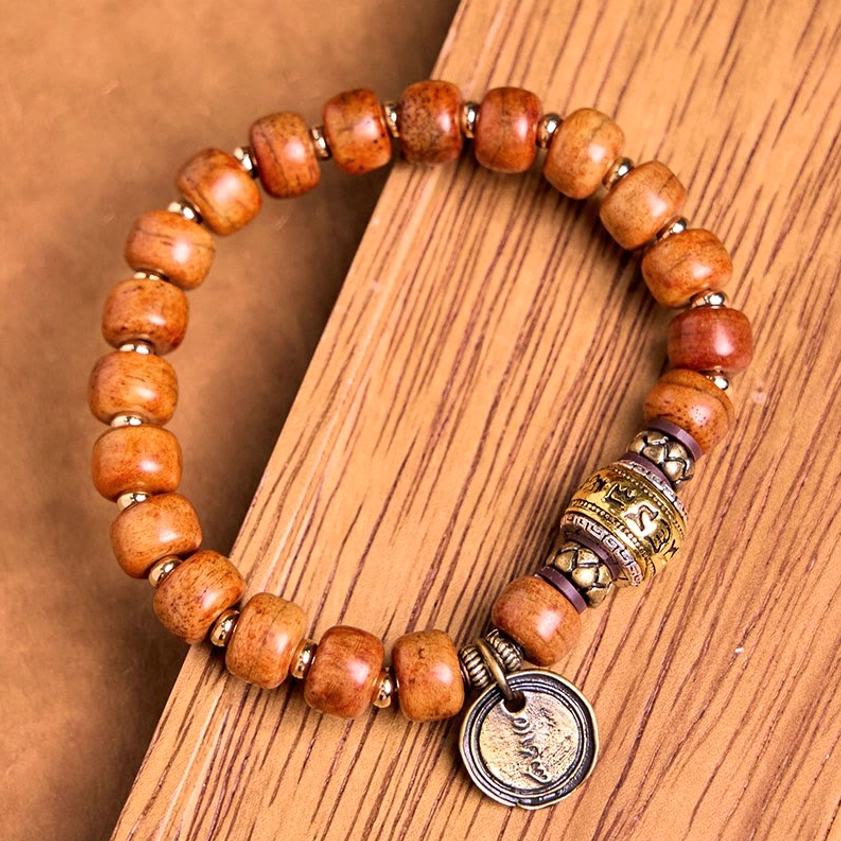 Angled side view of Buddhist OM prayer bracelet on wooden tabletop, showcasing reddish-brown natural bone beads with metal spacer accents