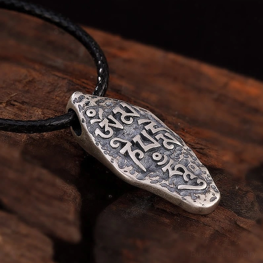 Tibetan Om Mani Padme Hum silver pendant front right oblique view, complete sacred mantra engravings with vintage metal patina on wooden board
