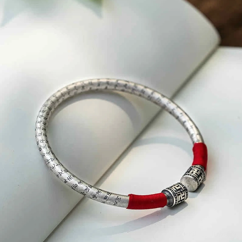 Om Mani Padme Hum open cuff bangle with engraved scripture and red silk wrap, overhead flat lay display