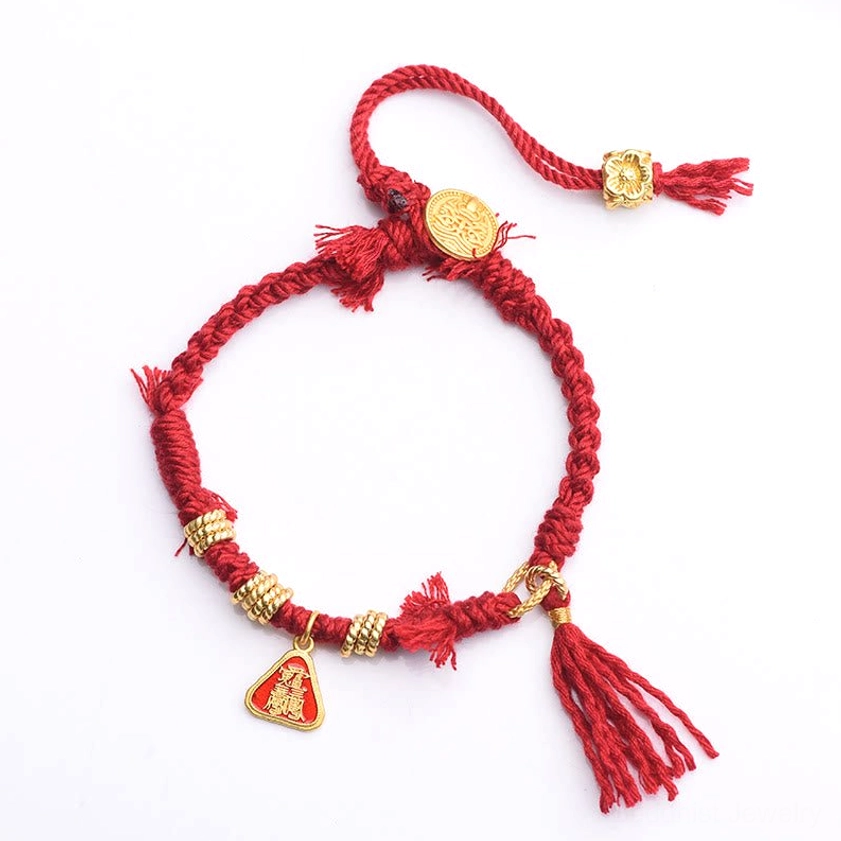 Tibetan style red string protection bracelet with braided cord, round gold charm, and flower tassel on beige tabletop