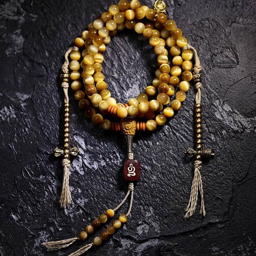 Full 108-bead Tiger Eye Mala with dual copper Vajra tassel counters and carved pendant charm, flat lay