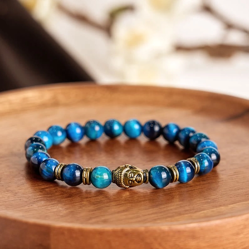 Close-up overhead view of multicolor tiger eye Buddhist bracelet with central gold Buddha charm on wooden tray