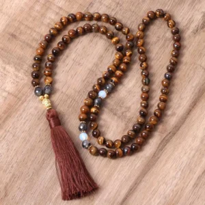 Tiger Eye Buddha mala tassel necklace with burgundy tassel displayed flat on wooden surface, showing loosely coiled golden-brown striped beads