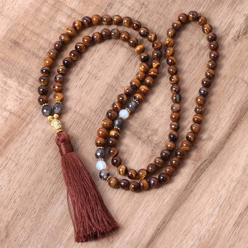 Tiger Eye Buddha mala tassel necklace with burgundy tassel displayed flat on wooden surface, showing loosely coiled golden-brown striped beads