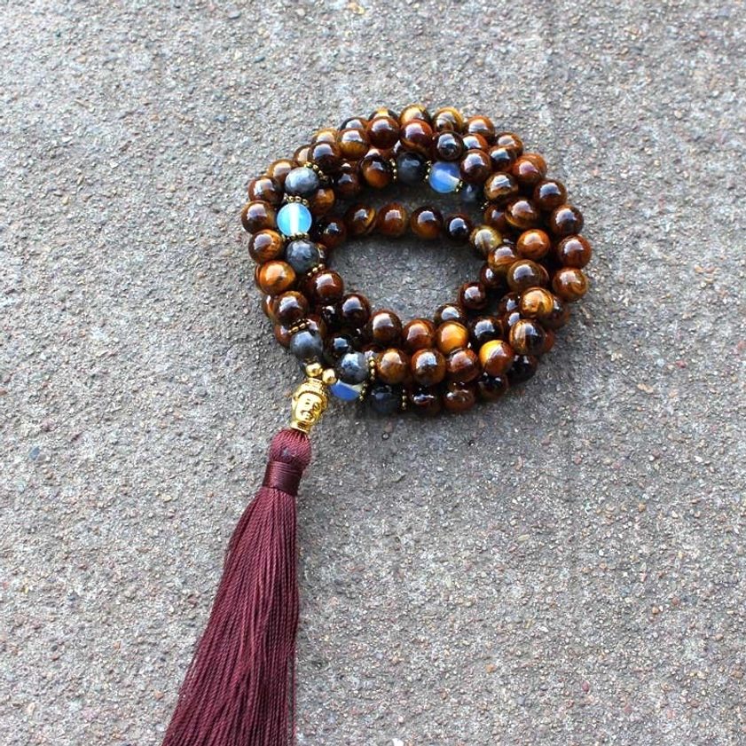 Tiger Eye Buddha mala necklace neatly coiled with burgundy tassel and metal Buddha charm on gray concrete background