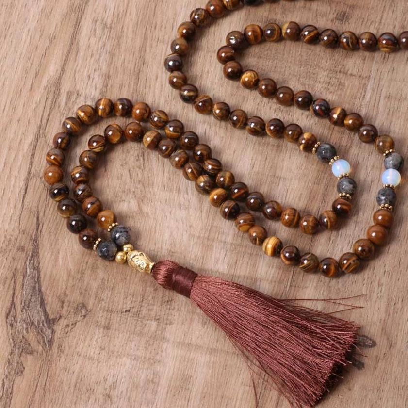 Tiger Eye Buddha necklace with deep red tassel arranged in curved layout on wooden tabletop, angled overhead perspective