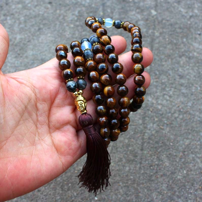 Hand-held view of Tiger Eye Buddha mala necklace in palm, showing Buddha head charm detail and dark tassel pendant