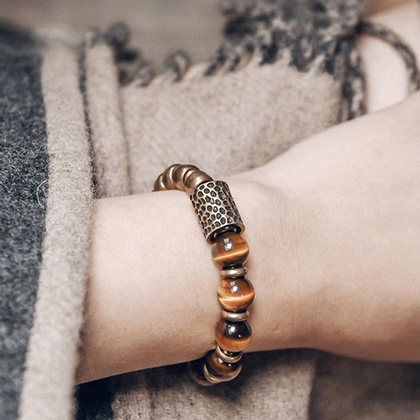 Hammered copper spacer accent and tiger eye beads on forearm, side view with stacked rings and beige scarf