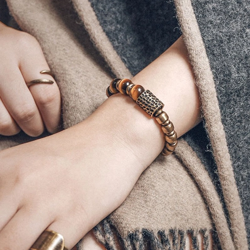 Tiger eye bracelet stacked with rings on right wrist, worn over beige scarf and grey coat, lifestyle shot