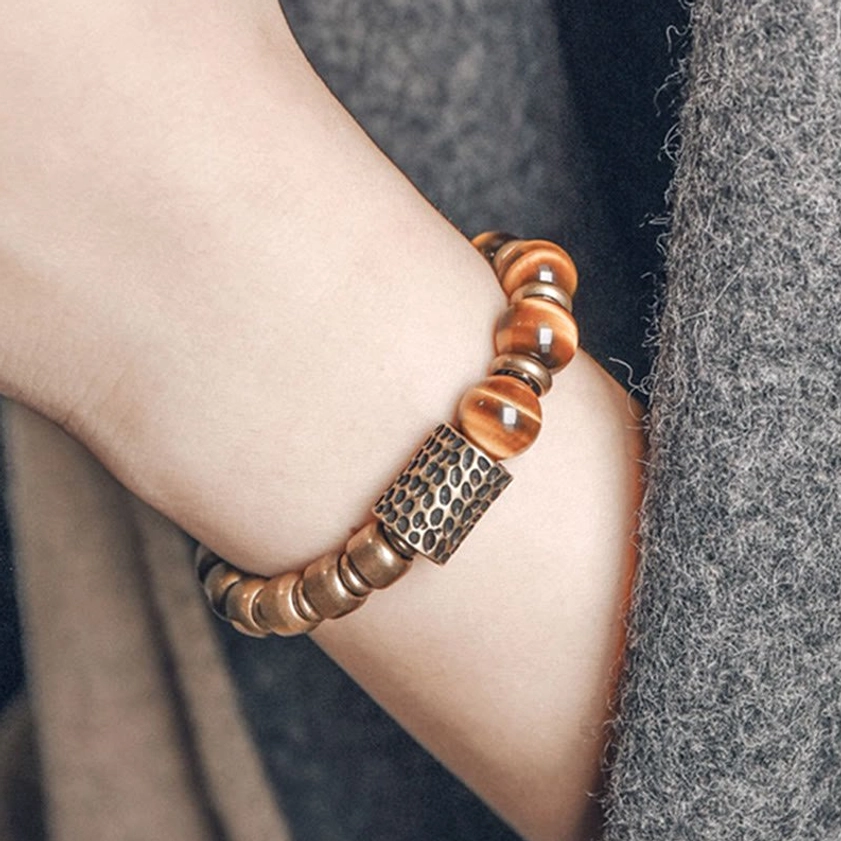Tiger eye stone copper protection bracelet worn on left wrist against grey woolen coat, side view