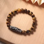 Tiger eye and nine-eye dzi bead protection bracelet with natural golden-brown striped beads on wooden display