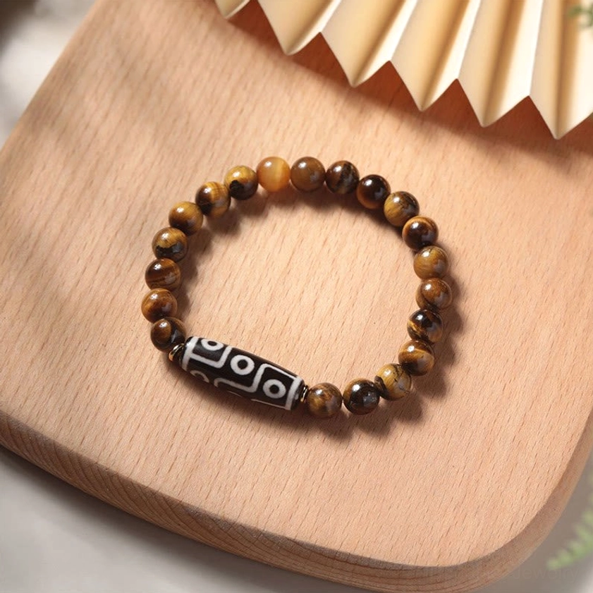 Tiger eye nine-eye dzi bead bracelet with polished striped beads displayed on wooden tray with fan decoration