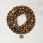 Tiger eye and lotus buddhist prayer mala beads flat lay top view with bronze lotus charm pendant and natural stone texture detail