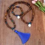 Tiger eye Buddhist mala beads set with blue accents and metal Buddha charm on wooden table