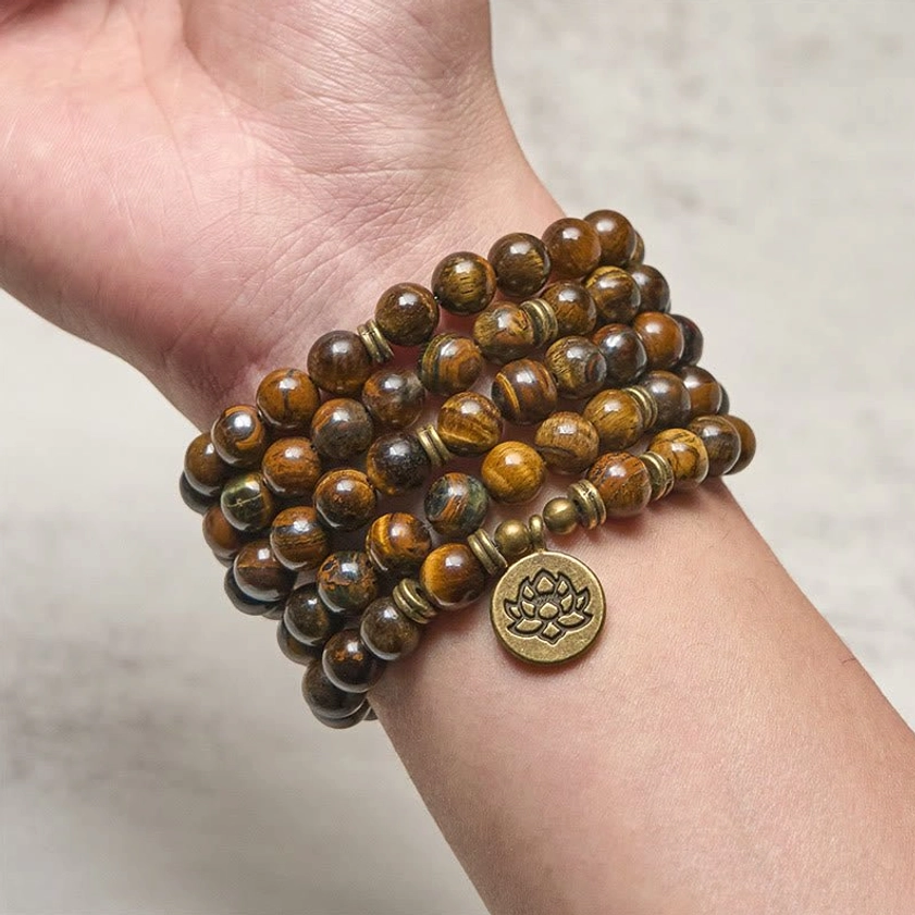 Multi-wrap tiger eye mala bracelet worn on wrist showing polished bead surface and bronze lotus pendant charm on human hand