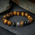 Tiger Eye and Black Obsidian Buddhist protection bracelet with silver Buddha charm displayed on dark stone background