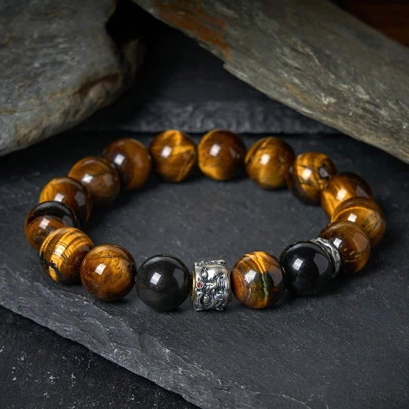Tiger Eye and Black Obsidian Buddhist protection bracelet with silver Buddha charm displayed on dark stone background