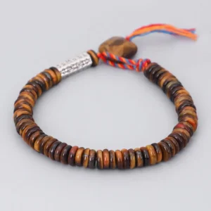 Tiger Eye Om Mani Padme Hum Buddhist protection bracelet with engraved silver charm and red-blue tassel, flat lay view on gray background