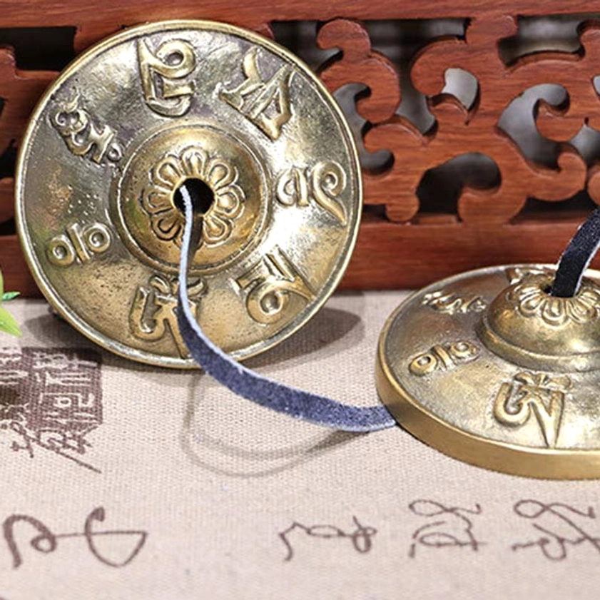 Close-up of tingsha cymbal showing detailed embossed om mani padme hum Sanskrit patterns and polished brass finish