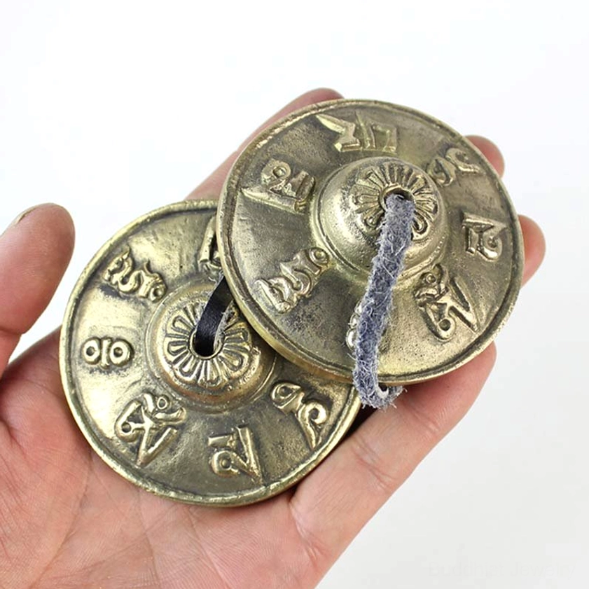 Hand holding Buddhist tingsha bell showing engraved design and leather tether connection