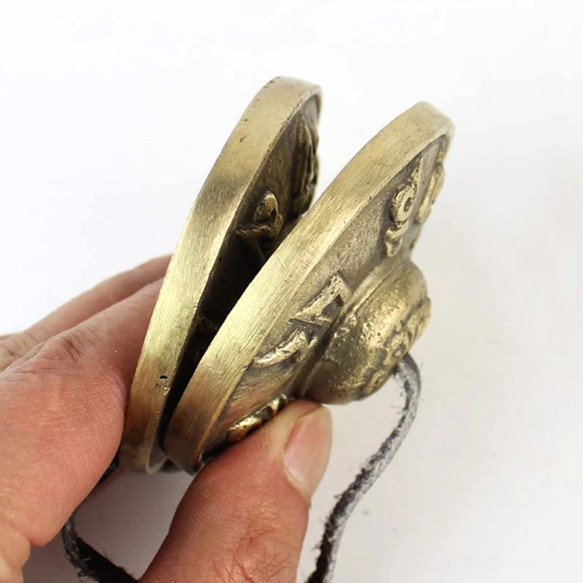 Side view of tingsha brass cymbals showing curved metal surfaces and leather strap detail