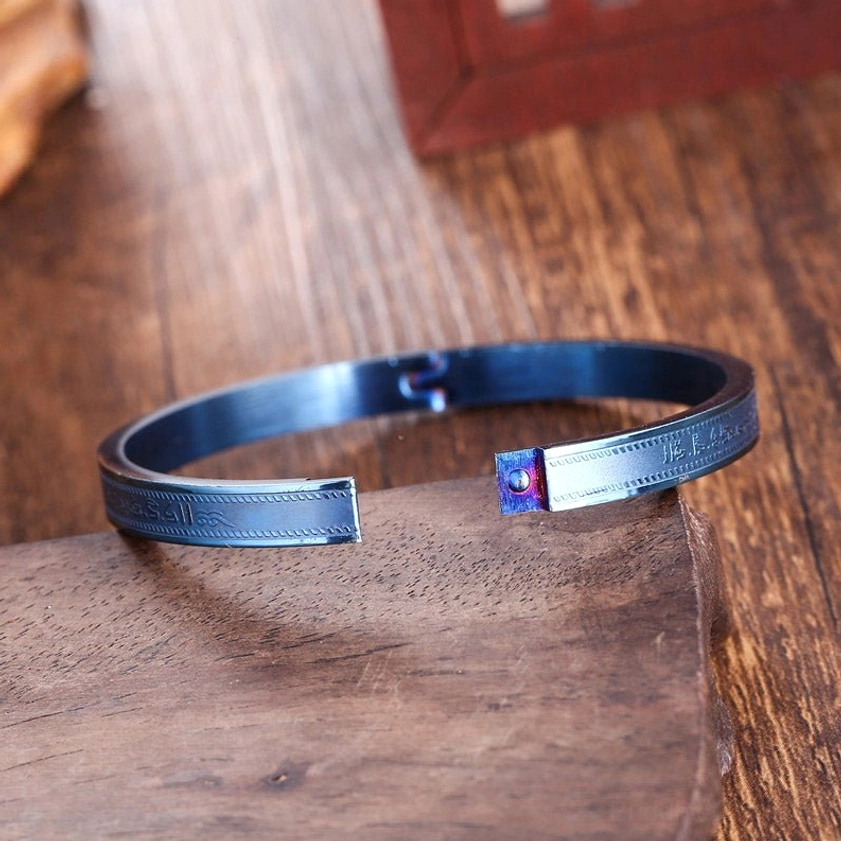 Burnt blue titanium steel blessing bracelet with subtle engraved textures visible on the band, side view on wooden surface