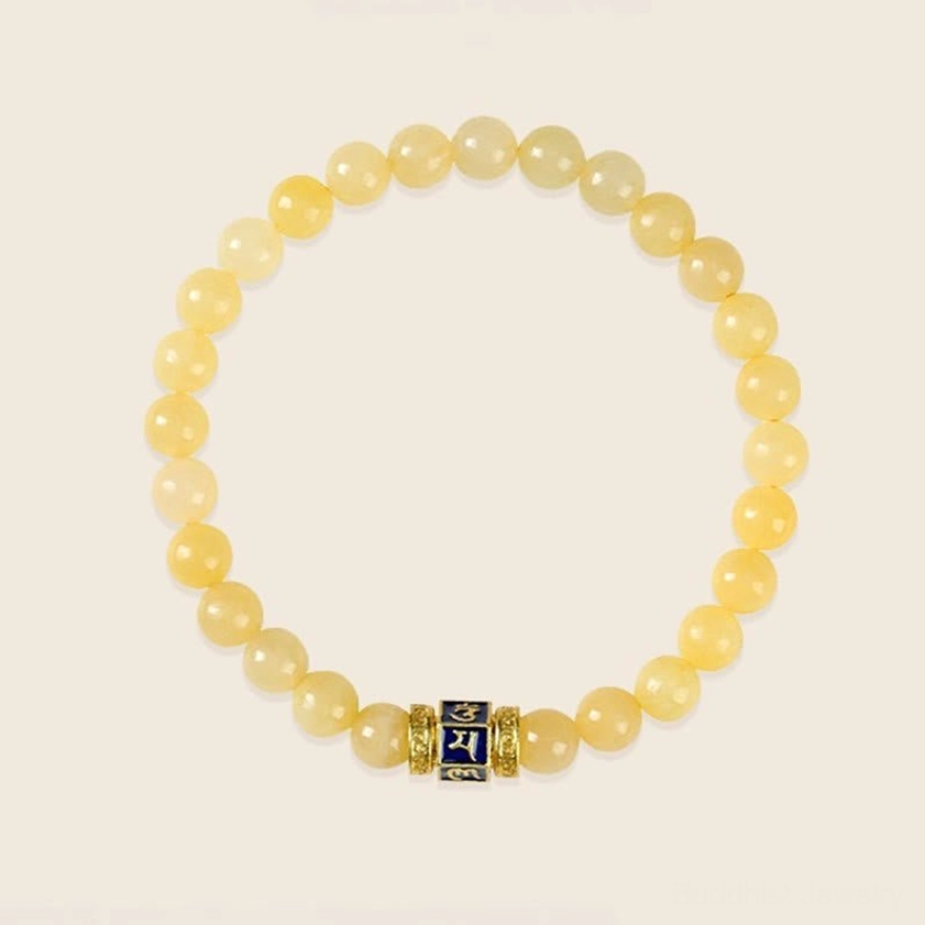 Uniform golden topaz beaded Buddhist bracelet with central engraved mantra charm on neutral background