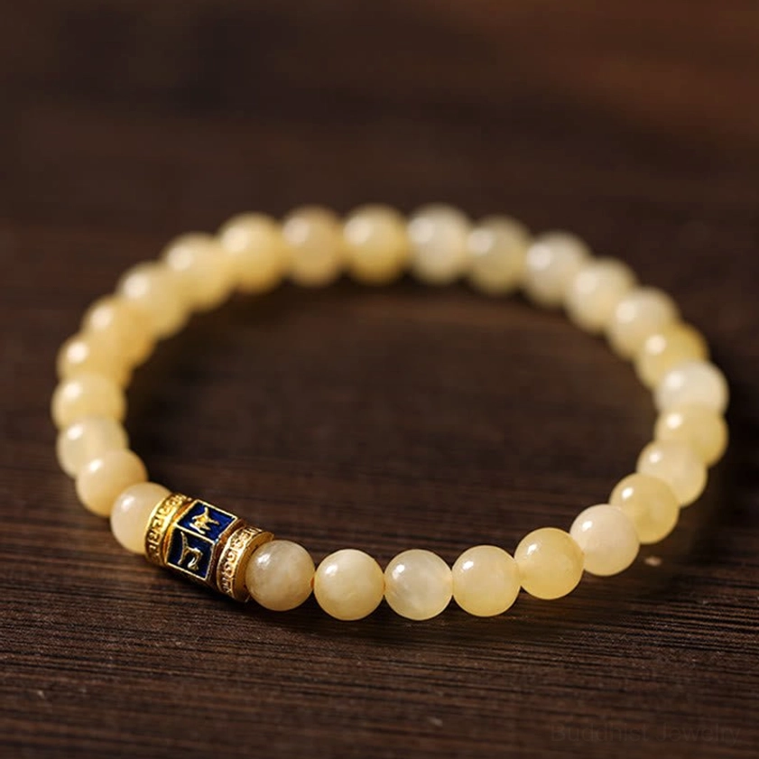 Close-up detail of topaz beaded mala bracelet with metal engraved mantra accent bead on wooden surface