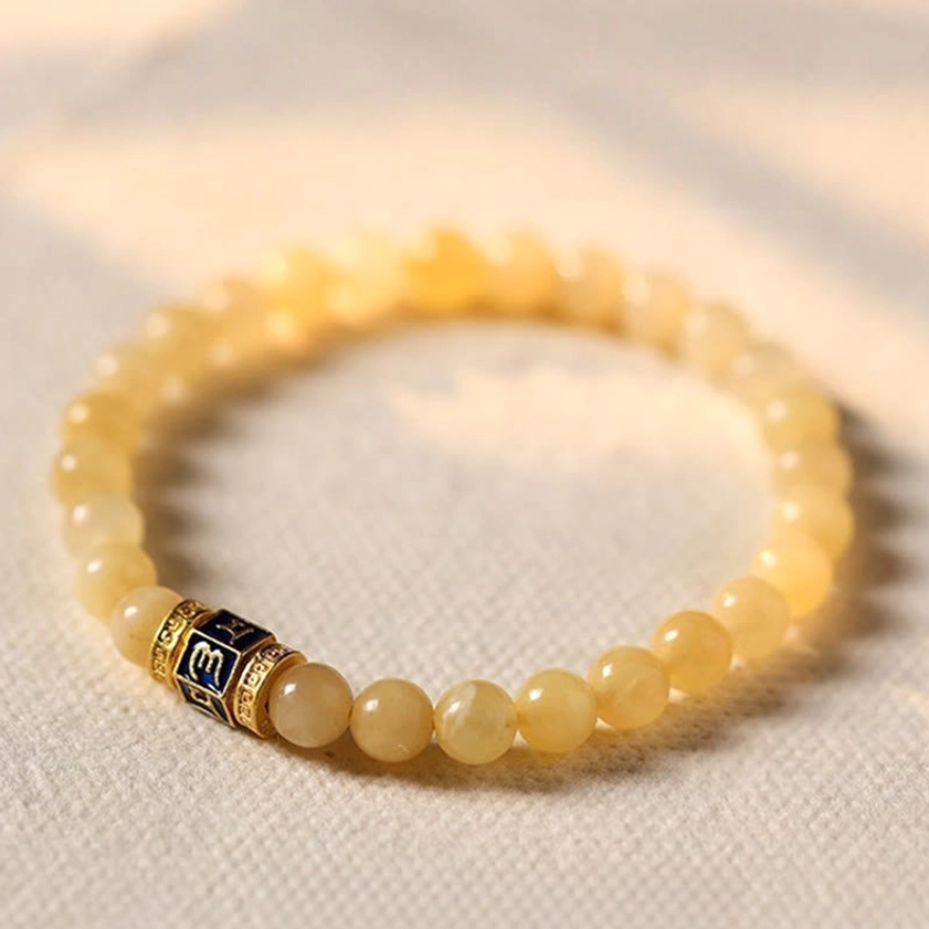 Golden topaz Om Mani Padme Hum Buddhist bracelet flat lay with engraved mantra charm on light fabric background