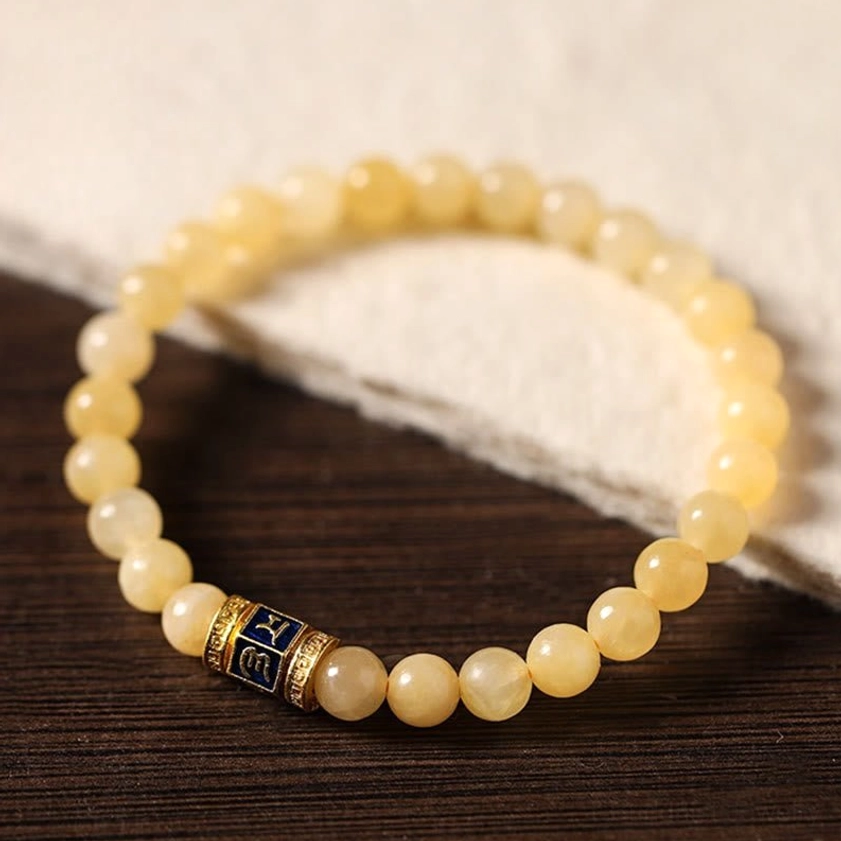 Angled overhead view of topaz Buddhist bracelet with warm yellow beads and engraved Om Mani Padme Hum charm