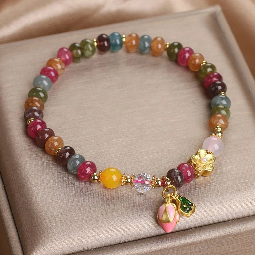 Tourmaline lotus wisdom bracelet showing multicolor beads, gold hardware, and pink lotus charm in luxury packaging
