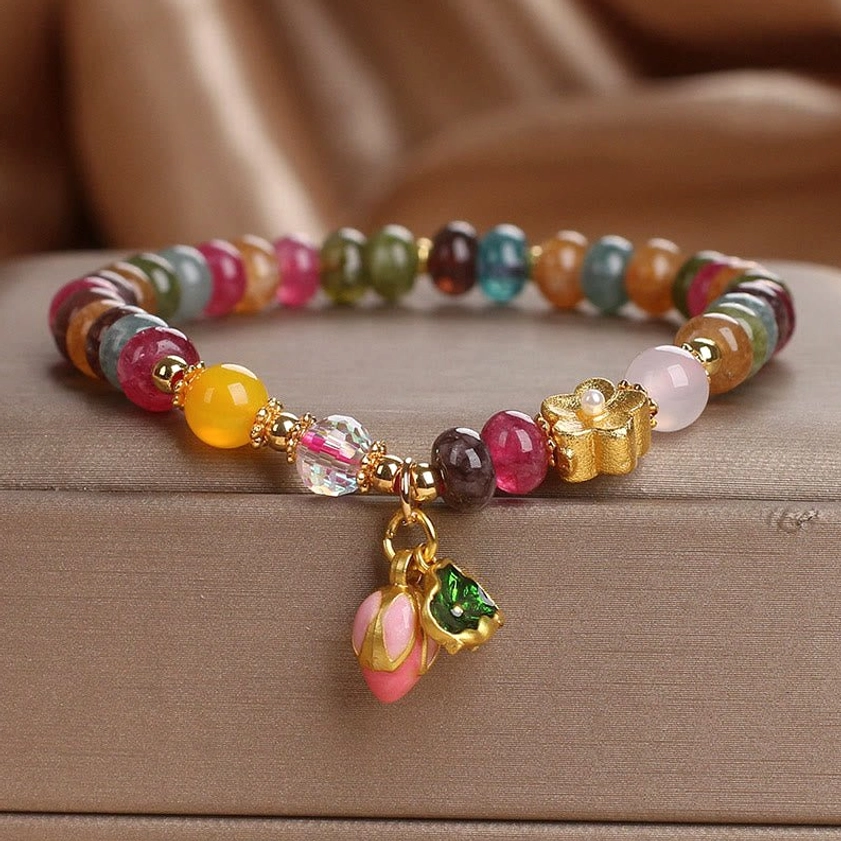 Tourmaline lotus seedpod wisdom bracelet with multicolor beads and pink lotus charm in luxury satin jewelry box, overhead view