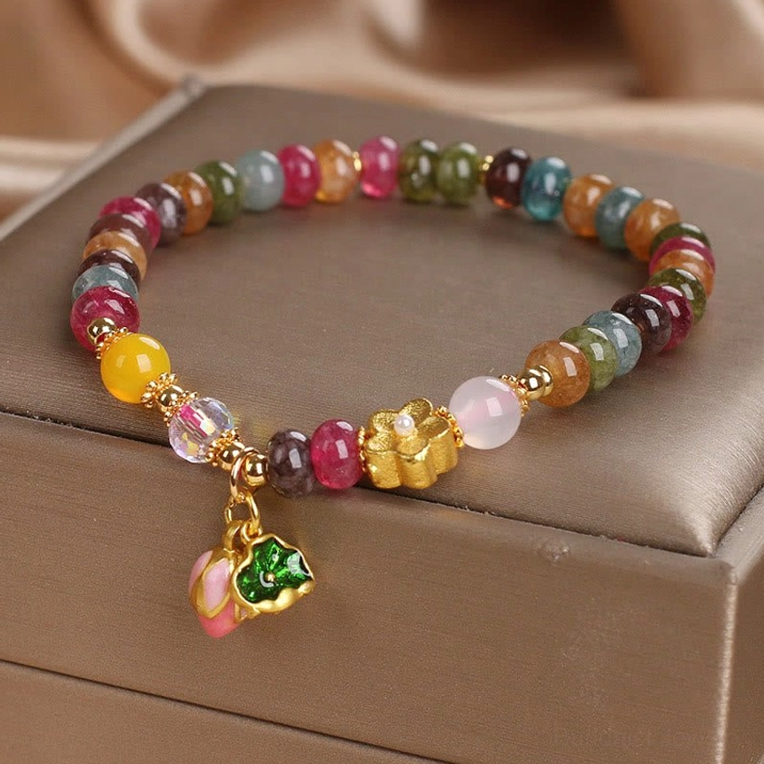 Multicolor tourmaline beaded stretch bracelet with gold hardware and pink lotus seedpod drop charm, flat lay display