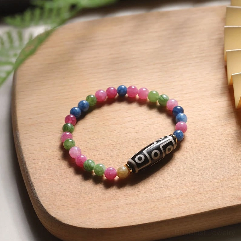 Tourmaline and nine-eye dzi bead protection bracelet with multi-color tourmaline stones on wooden surface