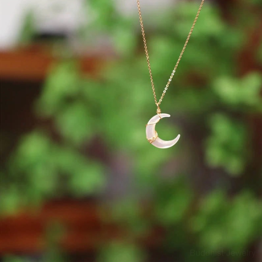 Delicate mini Tridacna crescent moon charm necklace hanging front view with thin gold chain against green natural background