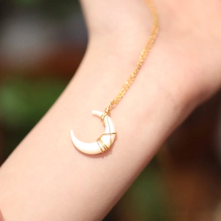 Crescent moon Tridacna stone Buddhist necklace worn on wrist, side view displaying elegant gold chain and pendant detail in outdoor setting